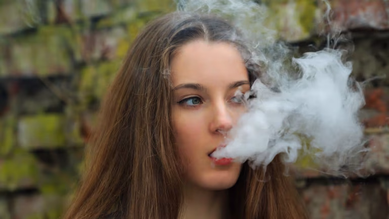 0_Vape-teenager-Young-pretty-white-girl-in-white-cardigan-smoking-an-electronic-cigarette-opposite-d.avif