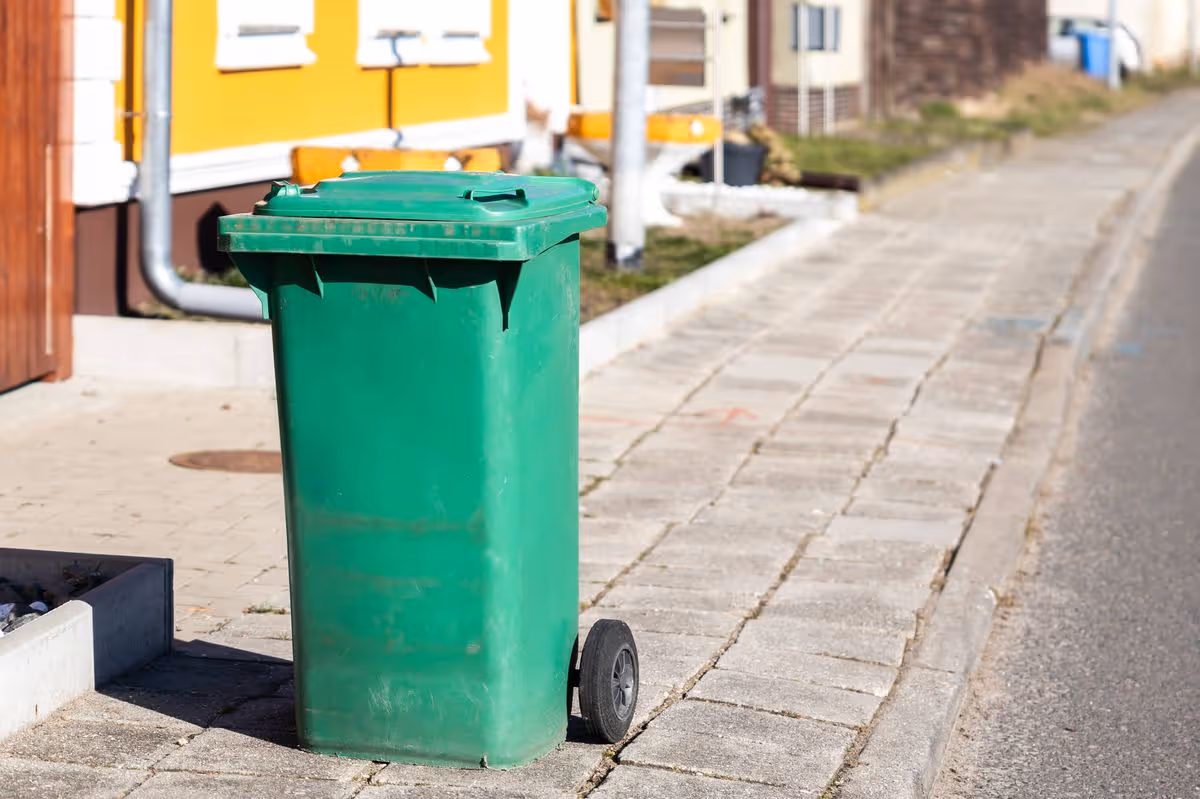 Green garbage can on the sidewalk in a residential area