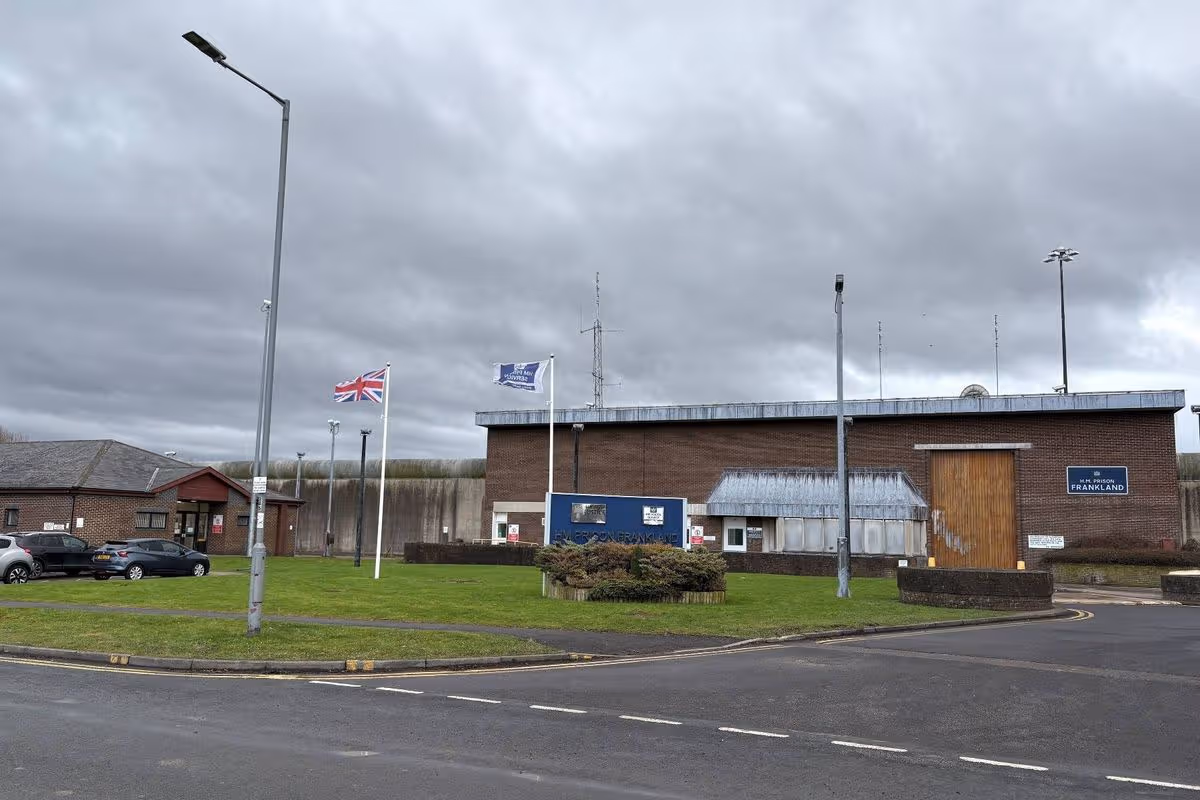 An image depicts an intersection with a building situated in the background. The building features multiple flags and a grassy area in front. Street lights and a road with white markings are visible. The sky is overcast.