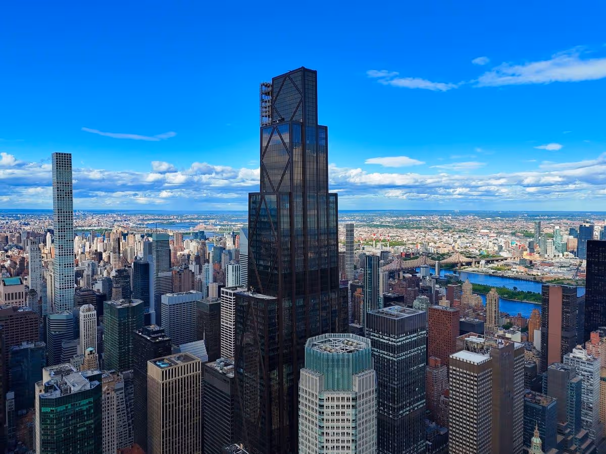 An aerial view of a densely populated urban area with numerous high-rise buildings and a clear blue sky in the background.