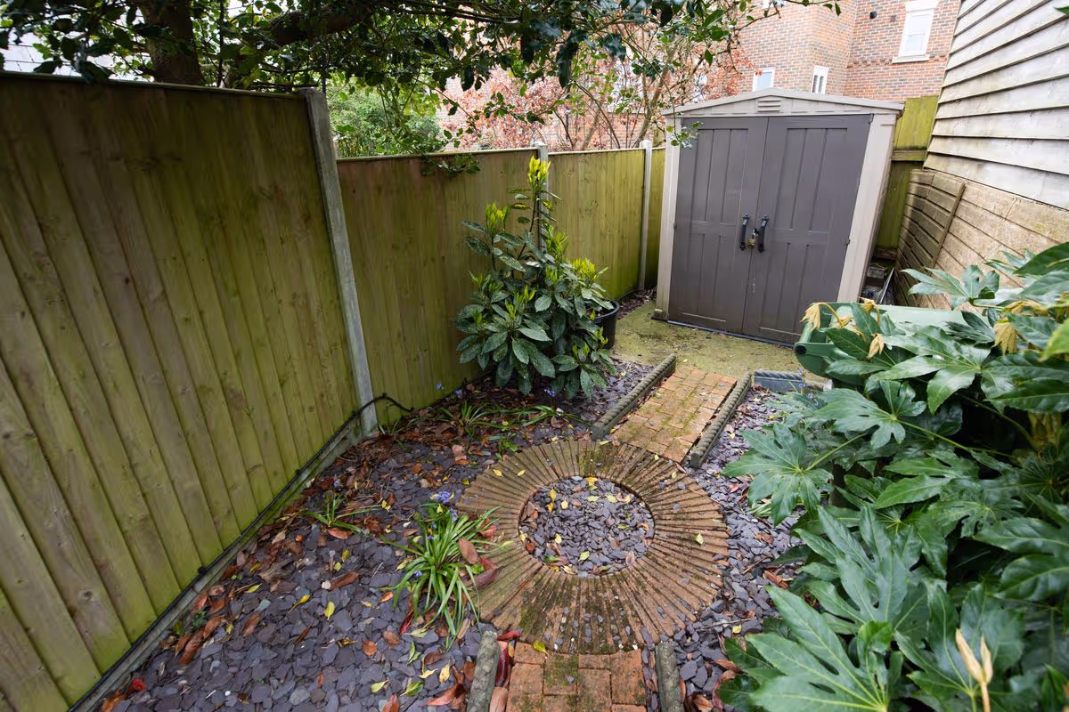 A general exterior view of a Plastic, Metal shed at the bottom of a courtyard back garden, with slate chippings, brick footpath and a round paving feature and timber fences