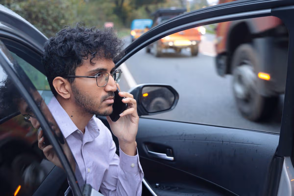 Young businessman uses mobile phone from broken car on highway, traffic blurred in distance, Saltash, Cornwall
