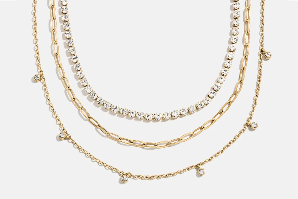 Three gold necklaces layered together, one with crystals, one a link chain, and one with small dangling crystals.