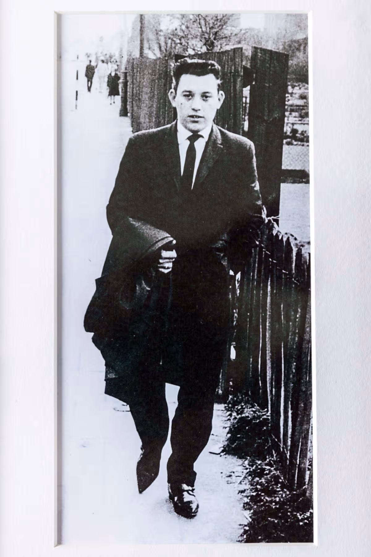 A black and white picture of David Whitby int he street wearing a suit and tie and carrying a coat
