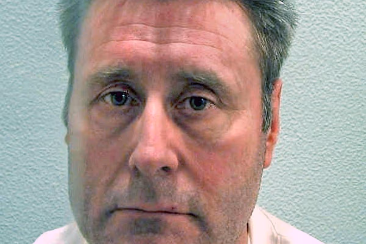 An adult male with gray hair, wearing a white shirt, is captured in a close-up portrait. The individual exhibits a contemplative expression, with visible furrows on the forehead and a slightly downturned mouth, suggesting a state of seriousness or concern. The background is a plain, light-colored wall, ensuring that the focus remains on the subject's facial features.