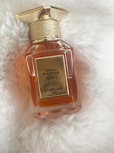 Guerlain Vanille Planifolia Extrait 21 perfume bottle on a white faux fur surface.