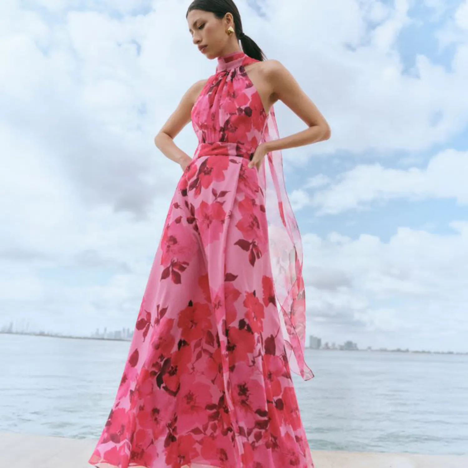 Woman in a pink floral print halter jumpsuit at the beach.
