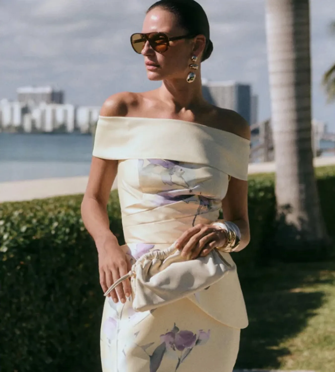 Woman in an off-the-shoulder floral dress, holding a clutch.