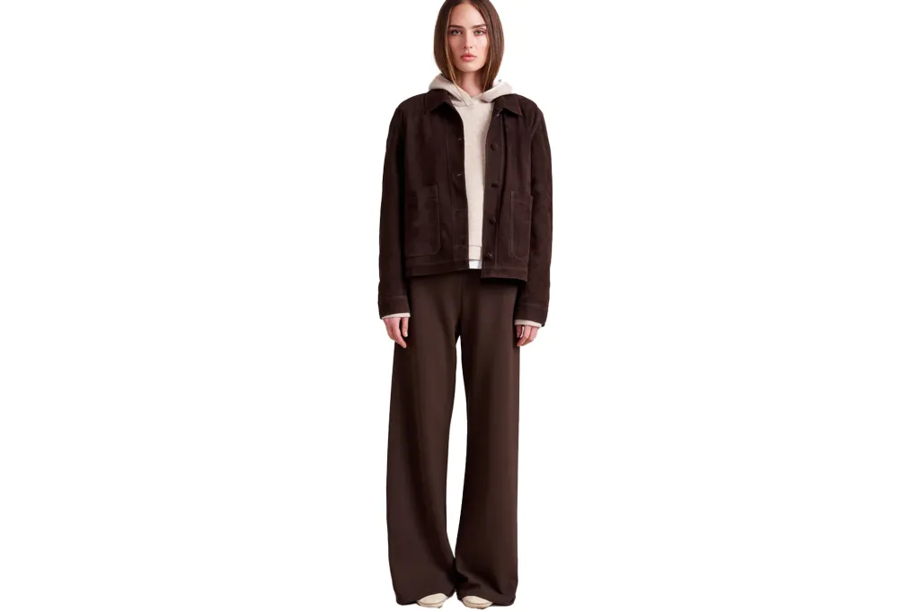 A woman models a brown suede jacket over a cream hoodie, paired with wide-leg brown pants and cream shoes.