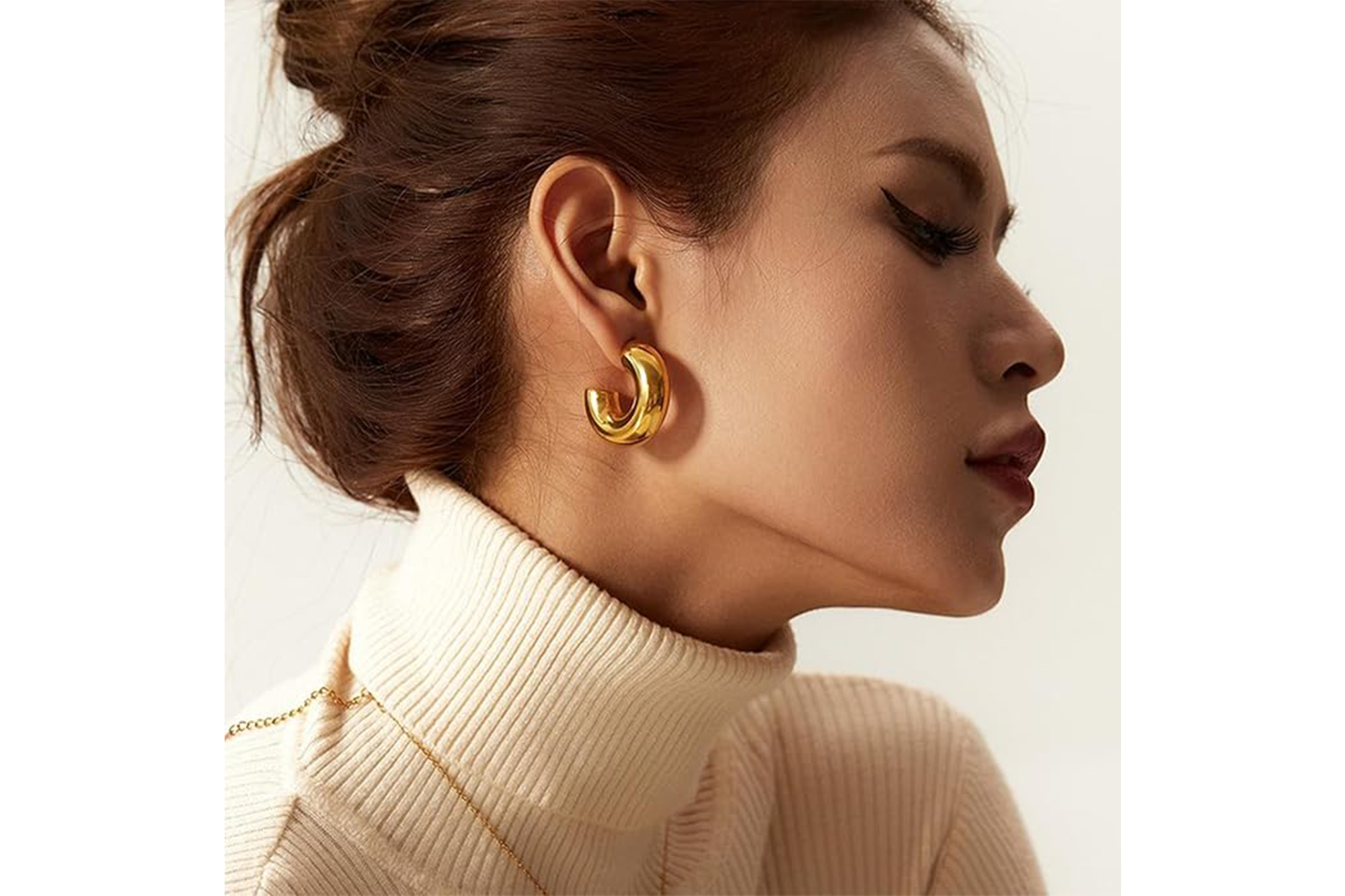 A woman wears a chunky gold hoop earring in her right ear.