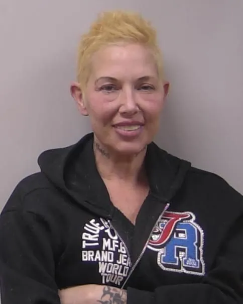 Mugshot of Kim Mathers, Eminem's ex-wife, smiling while wearing a black hoodie.