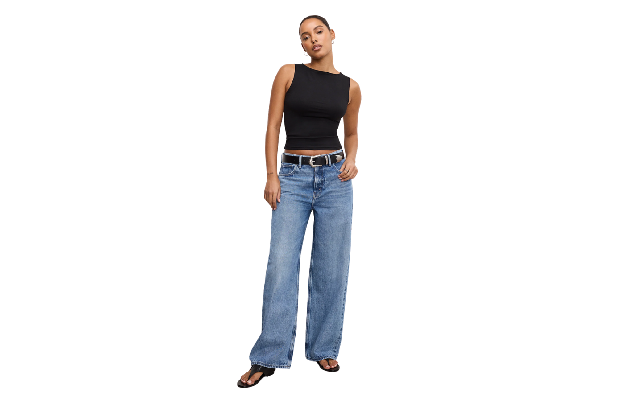 A woman wears a black sleeveless top, light blue baggy jeans, and black sandals.