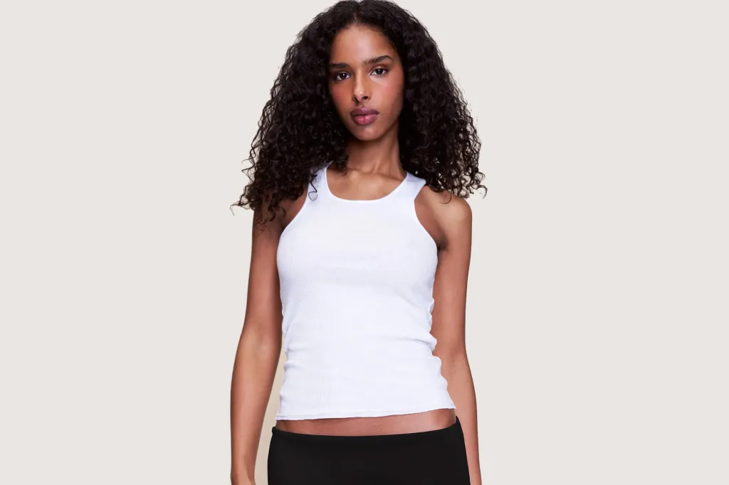 A woman with dark curly hair wearing a white tank top and black shorts.