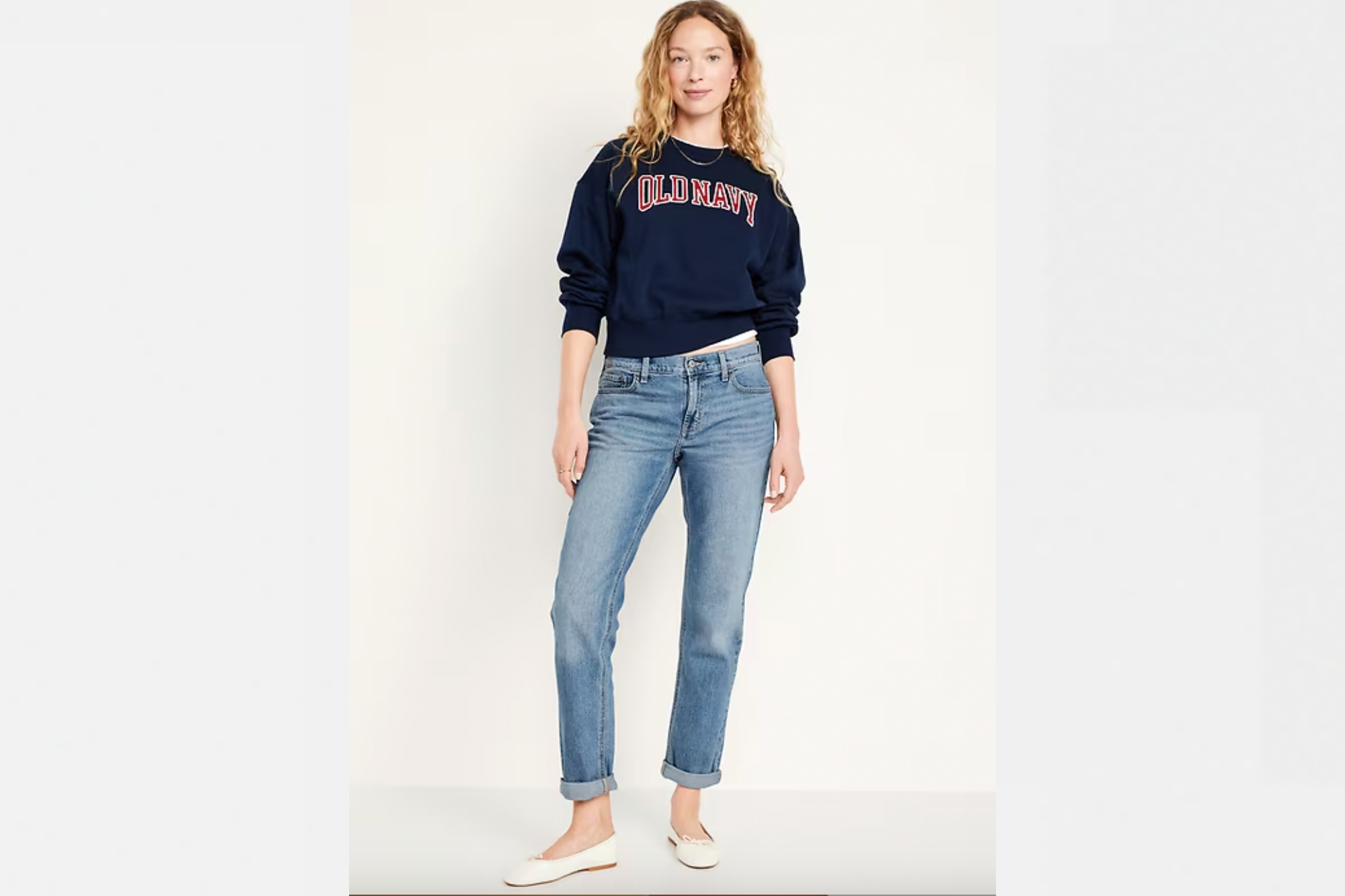 A woman in a navy blue Old Navy sweatshirt, light wash jeans, and white flats.