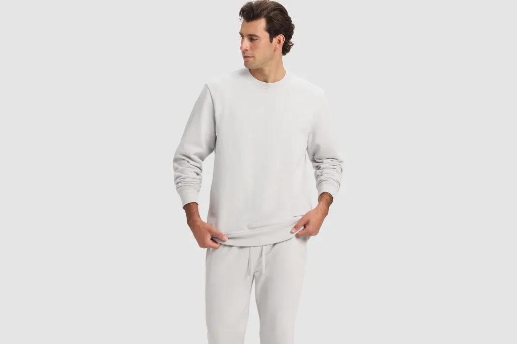 A man models a light grey crewneck sweatshirt and matching sweatpants.