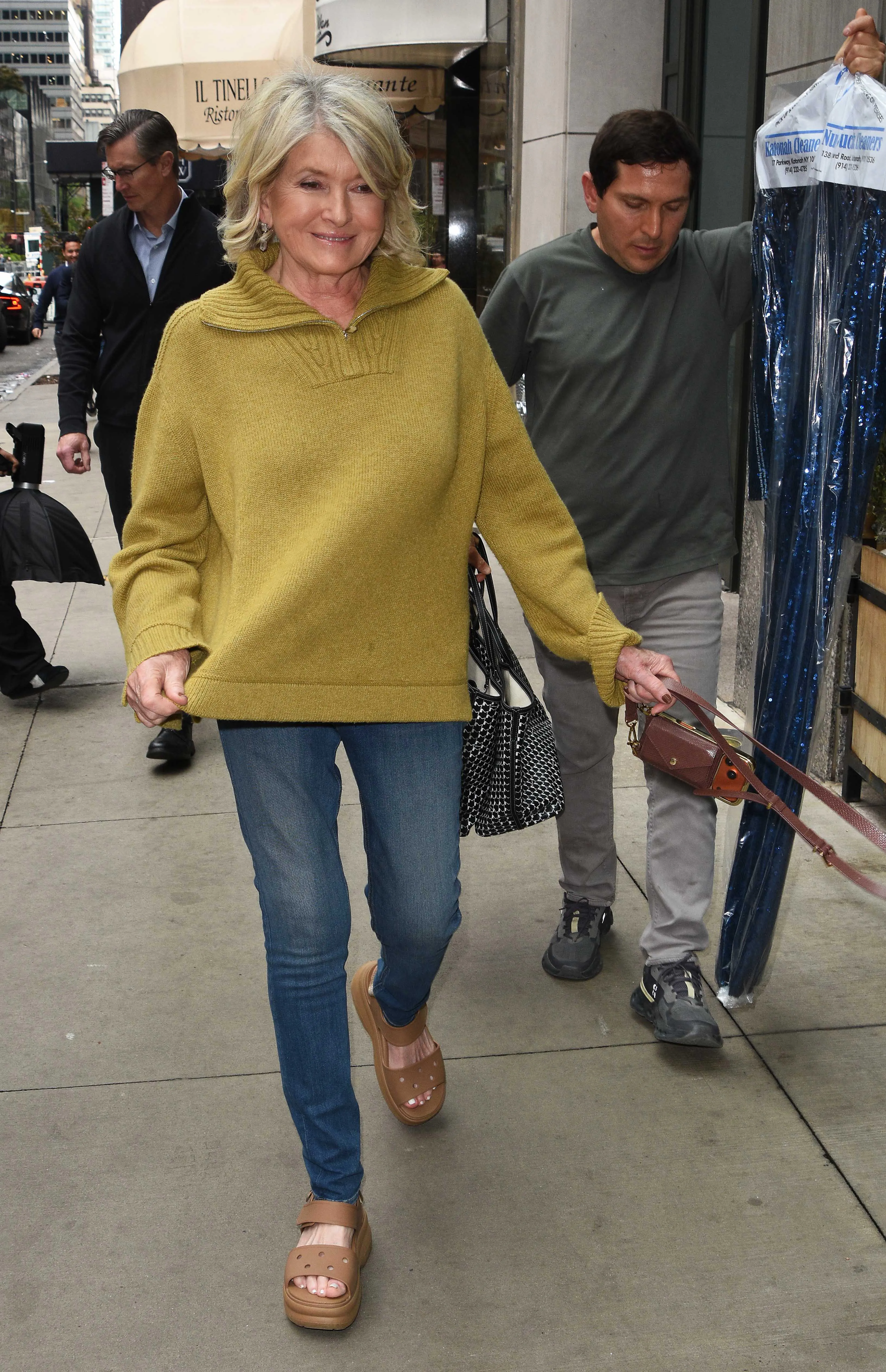 Martha Stewart wearing a chartreuse sweater, jeans, and brown platform sandals while walking on a city street.