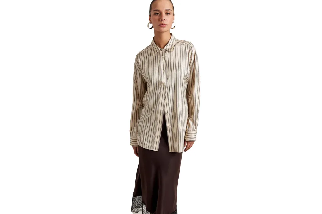 A woman in a cream striped button-up shirt and a black satin skirt with a lace trim.