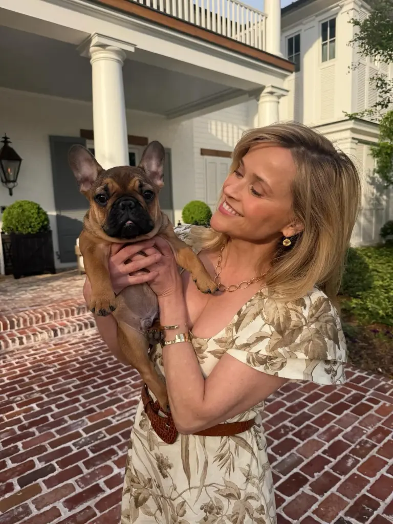Reese Witherspoon holding a French bulldog puppy.