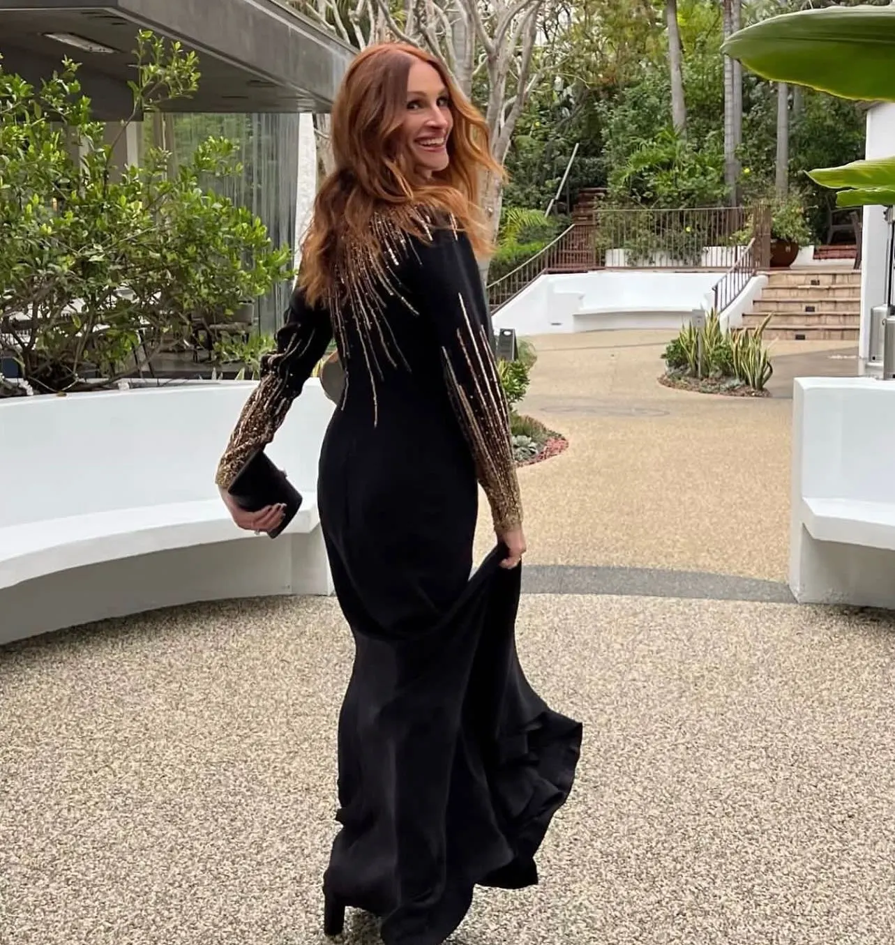 Julia Roberts in a long black dress with gold detailing on the sleeves, looking back and smiling.