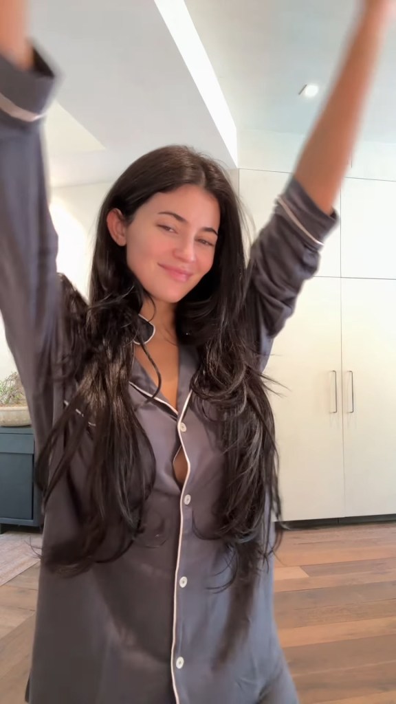 Kylie Jenner in gray pajamas with arms raised.