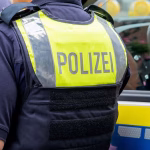 1_German-police-officer-seen-from-behind-in-a-yellow-vest-with-Polizei-text-standing-by-patrol-car-S.avif