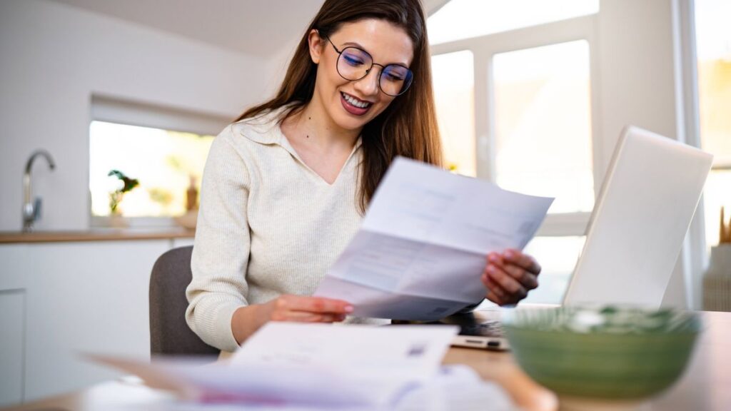 1773811130_0_Young-Smiling-Woman-With-Eyeglasses-Managing-Financial-Statements-at-Home-in-Front-of-a-Laptop.jpg