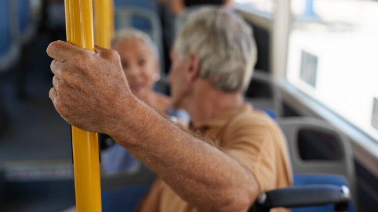 1774247314_0_Close-up-of-senior-man-holding-on-to-bar-on-public-bus.jpg