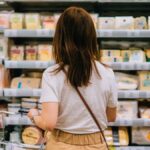 1775000327_0_Rear-view-of-young-woman-carrying-shopping-basket-choosing-cheese-standing-in-front-of-produce-ais.jpeg