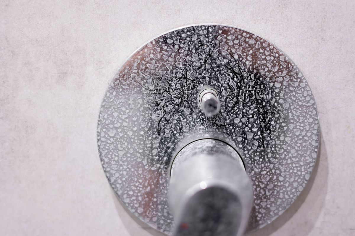 Dirty calcified shower mixer tap, faucet with limescale on it, plaque from hard water, Chrome plated shower, close up photo. Bathroom with grey tiles interior