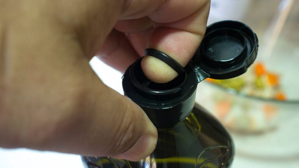 1776407291_1_Finger-opening-a-sealed-olive-oil-bottle-with-an-inner-pull-off-plastic-tab-underneath-the-cap.jpg