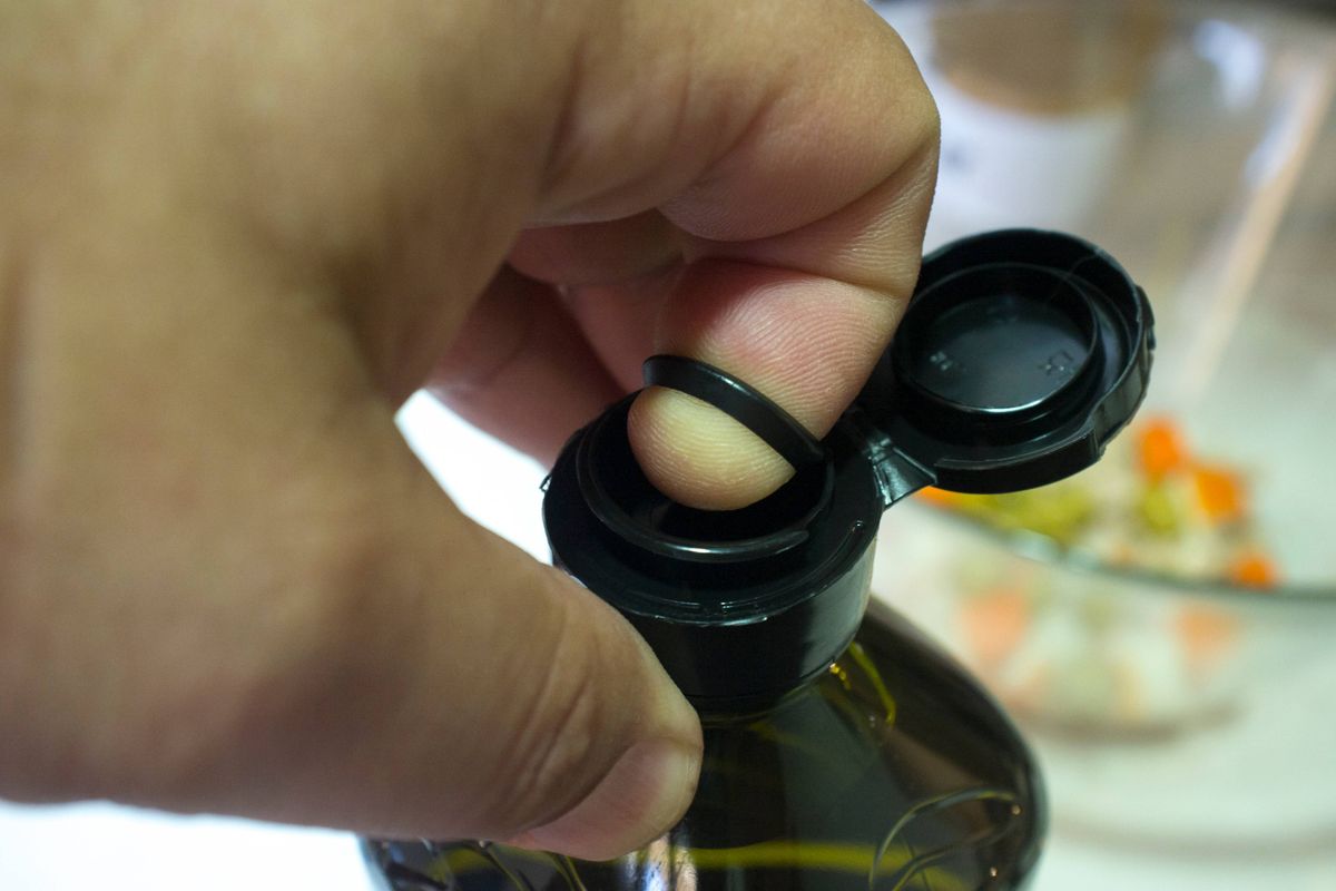 Finger opening a sealed olive oil bottle with an inner pull-off plastic tab underneath the cap. Closeup